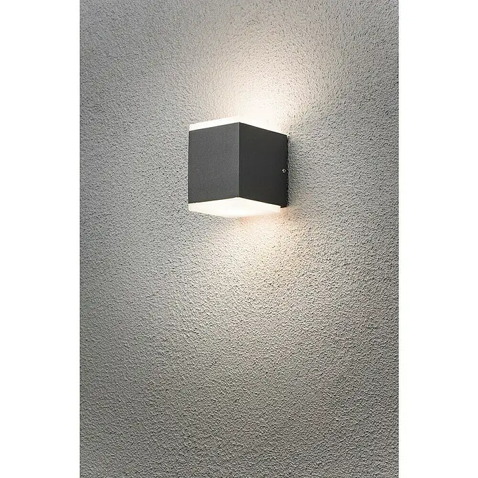 Konstsmide Außenwandleuchte - 12 W, 9 x 6 x 15 cm, Schwarz, IP54 - Schwarze, würfelförmige Wandleuchte mit Licht, das nach oben und unten scheint, montiert an einer grauen Wand mit Textur.
