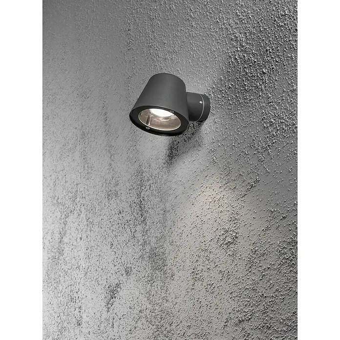 Konstsmide Außenwandleuchte - 35 W, 9 x 6 x 17 cm, Schwarz, IP44 - Eine Nahaufnahme einer modernen, grauen Außenwandleuchte, die an einer strukturierten grauen Wand befestigt ist und ein warmes Licht ausstrahlt.