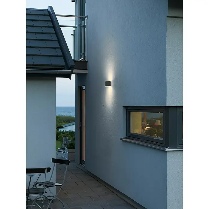 Konstsmide Außenwandleuchte - 12 W, 9 x 6 x 15 cm, Schwarz, IP54 - Moderne Hausfassade mit quadratischer Außenleuchte, die ein warmes Licht abstrahlt und die Architektur betont. Elegantes Design für stilvolle Beleuchtung.