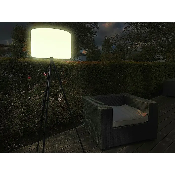 Müller-Licht Tint LED-Stehleuchte Khaya - Höhe: 143 cm, RGBW - Moderne Stehleuchte im Außenbereich. Die Lampe leuchtet hell und steht neben einem Rattansessel auf einer Holzterrasse.