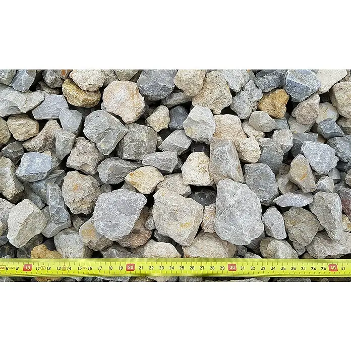 BHS Mallorca Big Bag de machaquilla - Grano: 20 mm - 40 mm, 900 kg, Gris - Primer plano de grava triturada de varios tamaños, medida con una cinta métrica amarilla para determinar el tamaño.