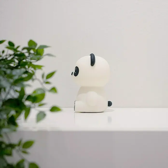 MegaLight LED-Nachtlicht PADDY PANDA - Weiß/Schwarz, L x B x H: 9 x 9 x 12 cm, RGBW, PADDY PANDA - Panda-Nachtlicht auf einem Regal neben einer Pflanze. Das sanfte Licht schafft eine beruhigende Atmosphäre.