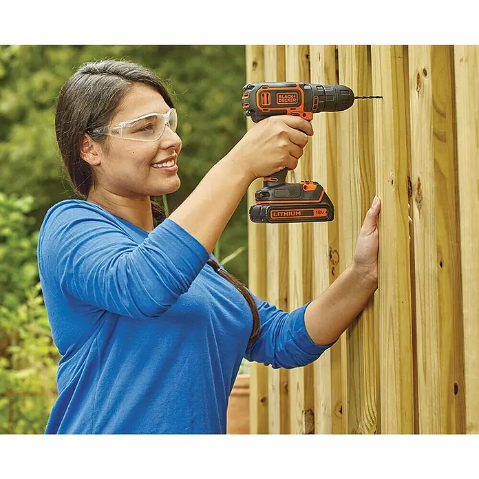 Black+Decker Akku-Bohrschrauber BDCDC18K-QW18 V, 1 Akku, 30 Nm - Frau bohrt mit einem Black+Decker Akku-Bohrschrauber Löcher in einen Holzzaun. Das Werkzeug ist handlich und leicht.