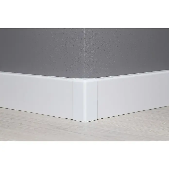 Außenecke Modern 58 - Weiß, 2 Stk. - Nahaufnahme von weißen Sockelleisten, die an einer grauen Wand befestigt sind und einen sauberen und modernen Look erzeugen.