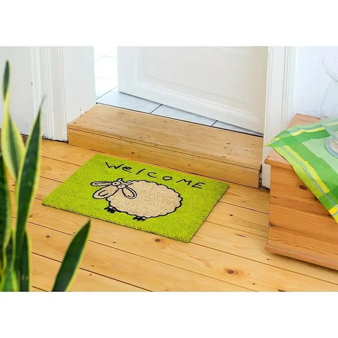 Astra Coco Fußmatte Style - 40 x 60 cm, Bunt, Material Nutzschicht: 100 % Kokos, Schaf, Kokos - Eine grüne Fußmatte mit einem Schaf und der Aufschrift "Welcome" liegt vor einer Tür auf einem Holzboden.