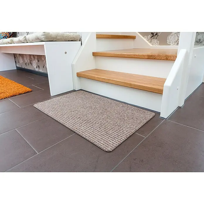 Astra Fußmatte Rib Line Sprint - 50 x 80 cm, Beige, 100 % Polypropylen - Fußmatte aus beigem Rippenstoff vor einer Treppe auf einem gefliesten Boden. Die Fußmatte ist rechteckig und hat eine subtile Textur.