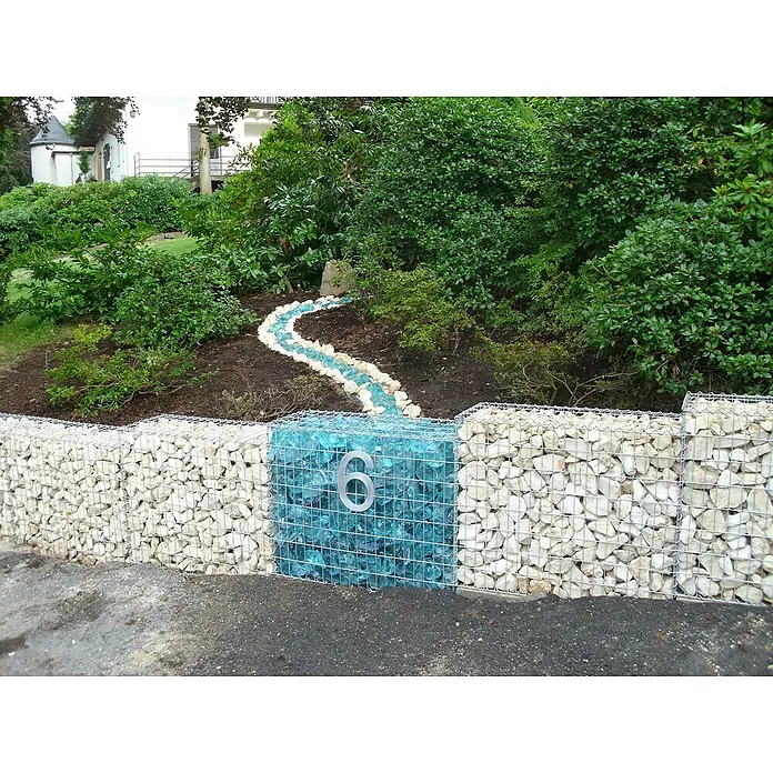Gabiona Gabione - 100 x 30 x 80 cm, Metall, Maschenbreite: 50 mm, Maschenhöhe: 100 mm - Hausnummer 6 auf einem Gabionenzaun mit weißen und blauen Steinen, eingebettet in eine grüne Gartenlandschaft.