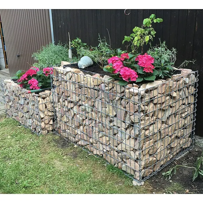 Gabiona Gabionen-Hochbeet130 x 80 x 80 cm, Metall, Maschenbreite: 50 mm, Maschenhöhe: 100 mm - Gabionen-Blumenkasten mit rosa Hortensien und verschiedenen Pflanzen. Der Kasten besteht aus Steinen, die von einem Drahtgitter gehalten werden.