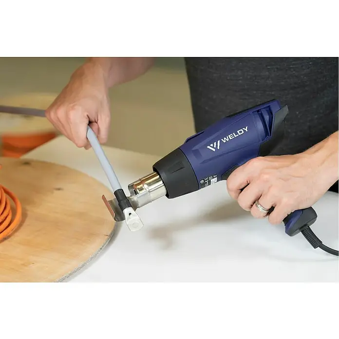 Weldy Heißluftgebläse HG 330-B - 1.600 W, Temperaturbereich: 350 °C - 550 °C - Ein Arbeiter verwendet eine WELDY Heißluftpistole, um ein Kabel zu bearbeiten, wobei der Fokus auf dem Werkzeug und seiner Anwendung liegt.