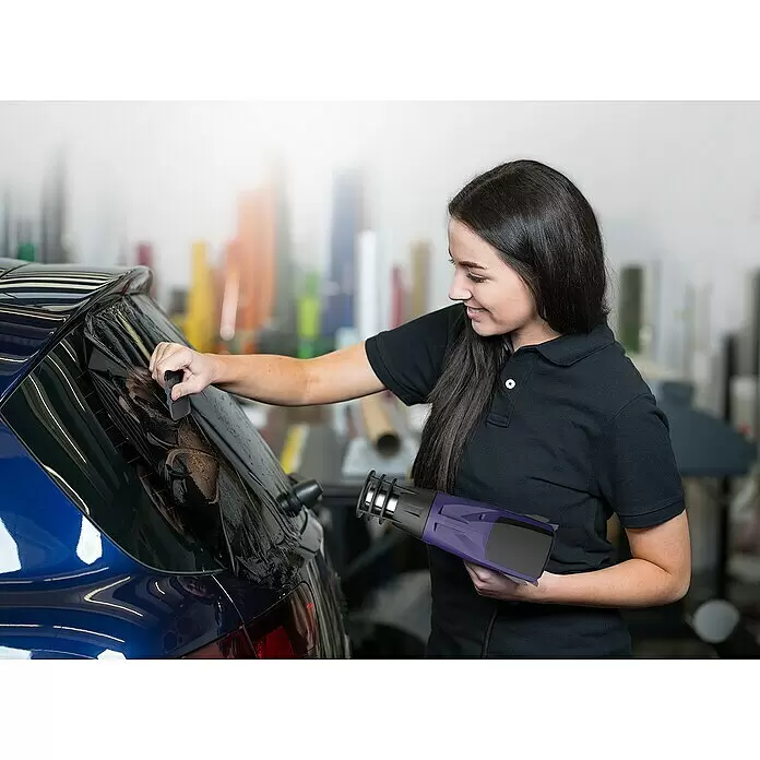 Weldy Heißluftgebläse HG 330-B Car-Wrap-Kit - 1.600 W, Temperaturbereich: 350 °C - 550 °C - Frau verwendet eine lila Heißluftpistole und Rakel, um Tönungsfolie am Heckfenster eines Autos anzubringen.