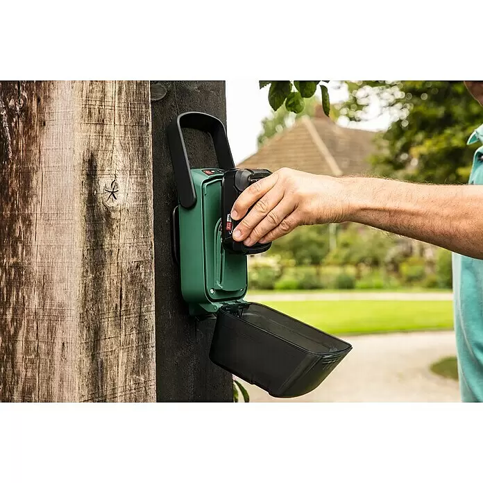 Bosch Power for All 18V Akku-Regenfasspumpe GardenPump 18V-2000 - 18 V, 1 Akku, Max. Fördermenge: 2.000 l/h - Eine Person setzt einen schwarzen Akku in ein grünes und schwarzes Gartenwerkzeug ein, das an einem Holzpfosten montiert ist.