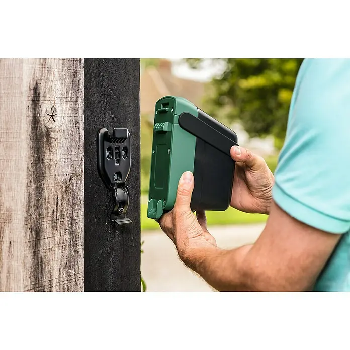 Bosch Power for All 18V WandhalterungPassend für: Bosch Akku-Regenwasserpumpe GardenPump 18 - Nahaufnahme einer Person, die eine grüne und schwarze Bosch-Bewässerungsbox an einer schwarzen Wandhalterung befestigt.