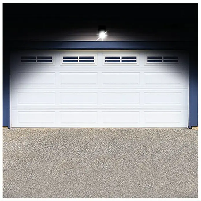 Foco solar Handy Brite - Sensor de luz - Primer plano de una puerta de garaje blanca con ventanas rectangulares debajo de una luz exterior brillante.