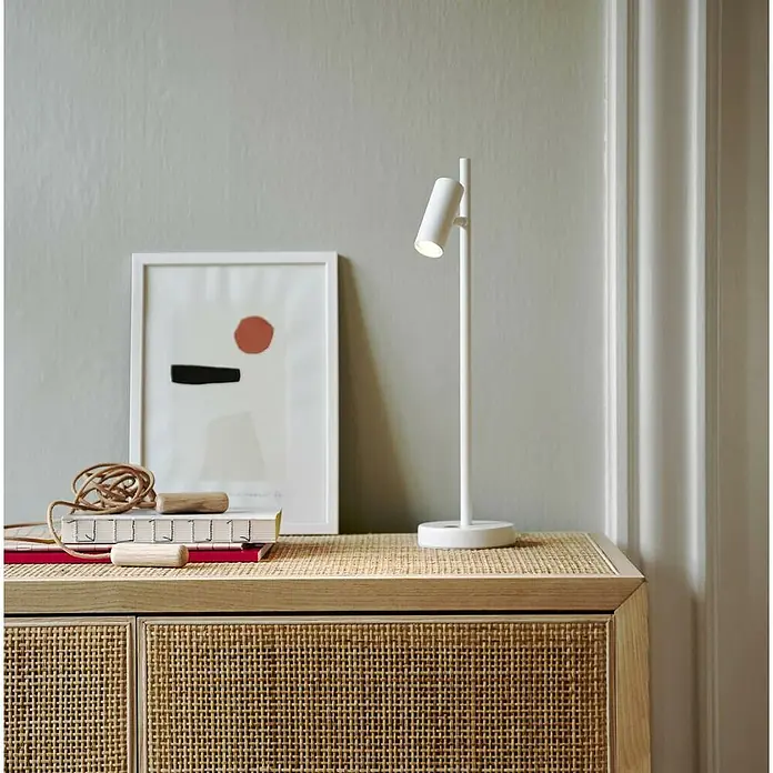 Nordlux Omari Lámpara de sobremesa LED - 3,3 W, L x An x Al: 10 x 15,5 x 40 cm, Blanco, Color de luz: Blanco cálido - Primer plano de una lámpara de mesa blanca colocada sobre un mueble con una impresión de arte abstracta al fondo.