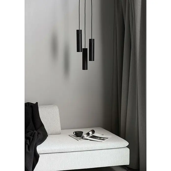 Nordlux Lámpara colgante Tilo - 45 W, Ø x Al: 6 x 22,6 cm, Número de bombillas: 3 ud., Negro, GU10 - Elegantes lámparas colgantes negras sobre un sofá luminoso con manta, taza y revistas, acentuado por cortinas grises al fondo.