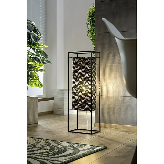 Stehleuchte40 W, Höhe: 76 cm, Schwarz - Elegante Stehlampe mit einem schwarzen, durchbrochenen Lampenschirm, die ein warmes Licht in den Raum wirft. Sie steht auf einem Teppich im Wohnzimmer.