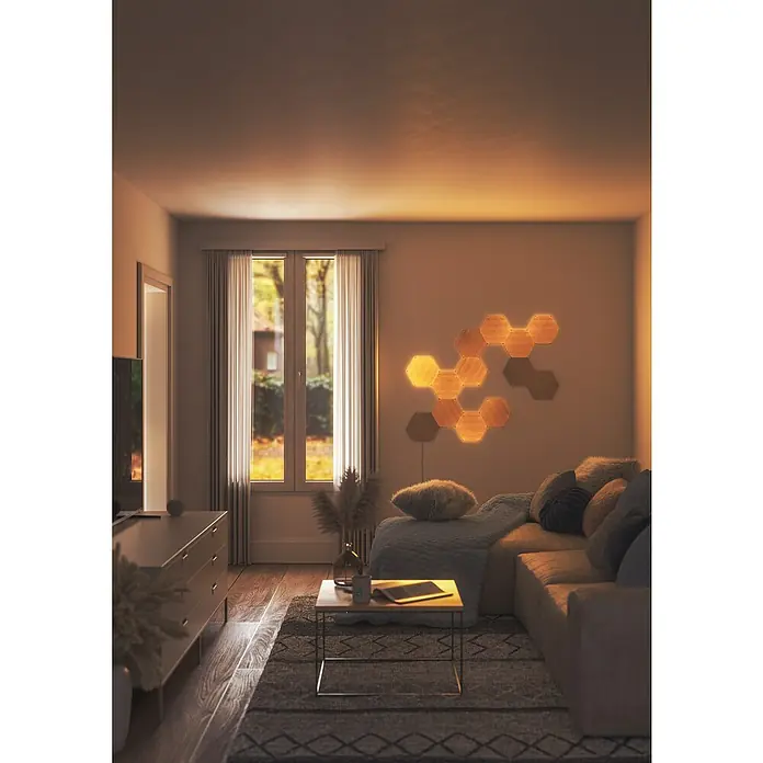 Nanoleaf Erweiterungskit Elements Hexagons 3 Panels - 42 W, Holzoptik, Mehrfarbig, Hexagons, Smart Home-fähig: Ja - Ein gemütliches Wohnzimmer mit einem stilvollen Sofa und einer einzigartigen, sechseckigen Wandleuchte, die für warmes Licht sorgt.