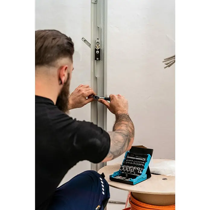 Hazet Steckschlüssel-Set SmartCase - 50 Stk. - Ein Mann befestigt ein Fensterteil mit Schrauben mit einem Werkzeug. Ein Werkzeugkasten befindet sich auf einem Tisch.