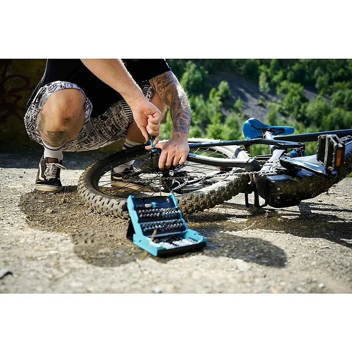 Hazet Bit-Set SmartCase - 69 Stk. - Nahaufnahme eines Mannes, der ein Fahrrad mit Werkzeug aus einem blauen Werkzeugkasten repariert, ideal für Reparaturen unterwegs.