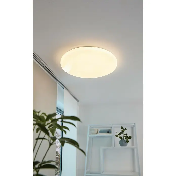 Eglo LED-Deckenleuchte rund POGLIOLA - 15 W, Ø x H: 31 x 5,5 cm, Weiß, Warmweiß - Das Bild zeigt eine runde, weiße Deckenleuchte, die hell leuchtet und den Raum erhellt. Im Hintergrund sind ein Fenster und ein Regal zu sehen.