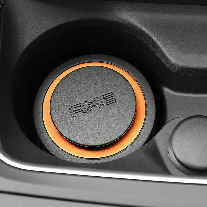 Axe Ambientador de coche Gel - Dark Temptation - Primer plano de un disco redondo "AXE" gris con un borde naranja, colocado en un recipiente negro.