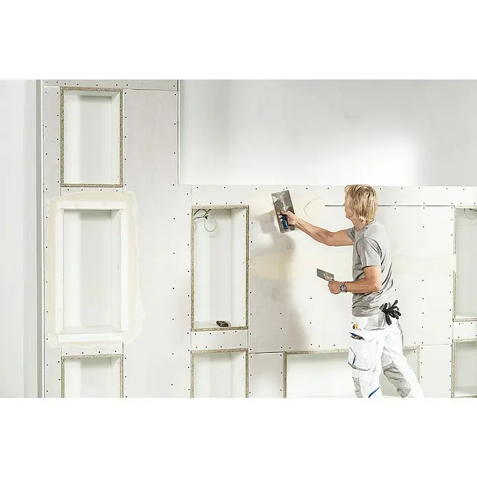 Knauf Wandnischen-Set M - 60 x 36,2 cm - Ein Mann spachtelt eine Wand mit eingebauten Regalen, wodurch eine glatte Oberfläche entsteht. Er verwendet Spachtelwerkzeuge für das Finish.