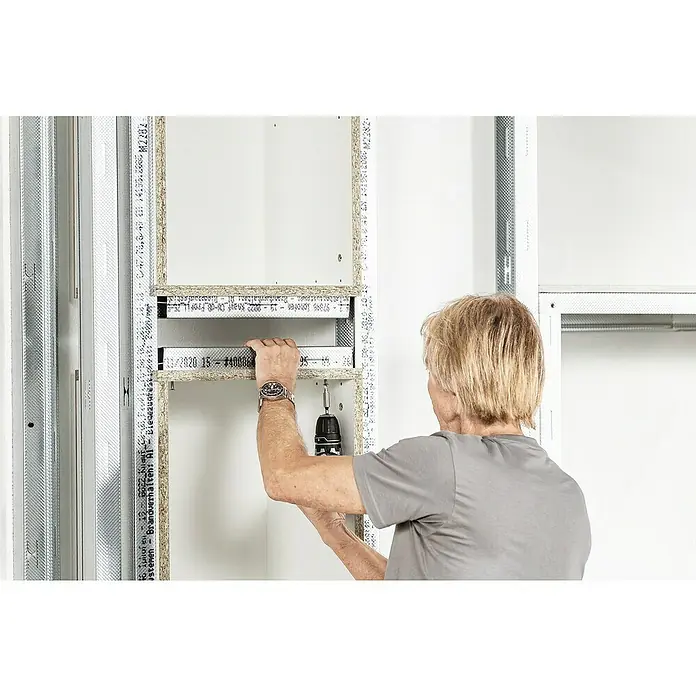 Knauf Wandnischen-Set L - 80 x 36,2 cm - Eine Person befestigt eine Metallschiene an einem Holzrahmen mit einem Akkuschrauber. Die Schiene ist Teil eines modularen Regalsystems.