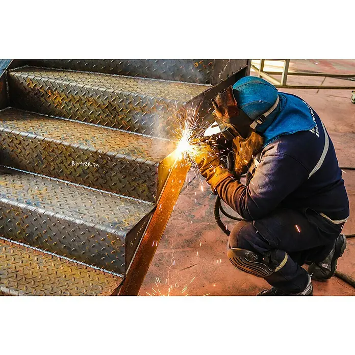 Gys Soldador combinado Easymig 150 - Corriente de soldadura: 20 A - 140 A - Un soldador trabajando en una escalera; se pueden ver claramente las medidas de seguridad que incluyen un casco y guantes.
