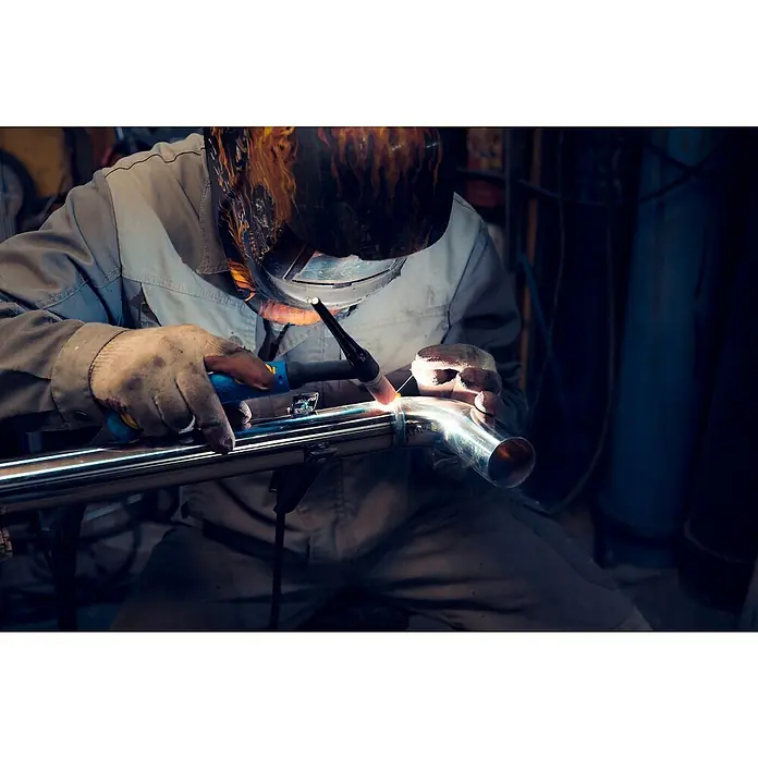 Gys Soldador combinado GYSMI E163 - Corriente de soldadura: 10 A - 160 A - Un soldador trabajando en un tubo de acero inoxidable con una máquina de soldar, usando guantes y máscara de protección.