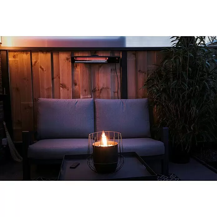 Sunred Wandheizstrahler Professional Royal Diamond - 2.500 W, Schwarz, 15,5 mm x 65 cm x 13 cm - Schwarzer Terrassenheizstrahler mit rotem Glühen, montiert an einer Holzwand über einem grauen Outdoor-Sofa.