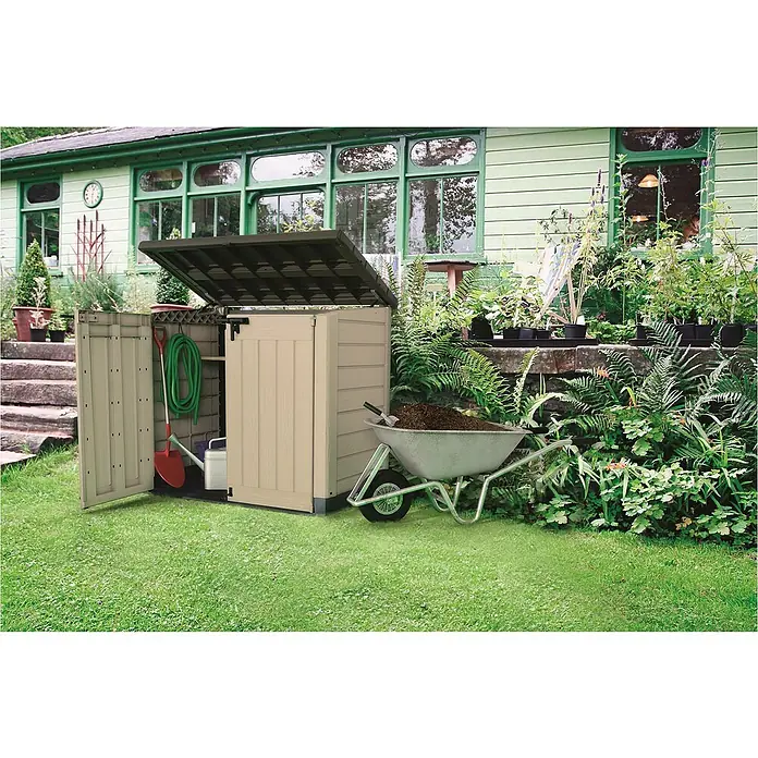 Keter Arcón Store it out Max - L x An x Al: 82 x 145,5 x 125 cm, Marrón - Cobertizo de jardín con puerta abierta llena de herramientas de jardinería, junto a una carretilla en un jardín.