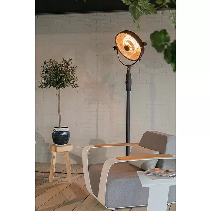 Sunred Halogen-Heizstrahler Retro - Höhe: 210 cm, 2.100 W, Schwarz - Schwarzer Heizstrahler mit beleuchtetem Element, neben einem modernen grauen Sessel mit weißem Rahmen, der ein warmes Lounge-Ambiente schafft.