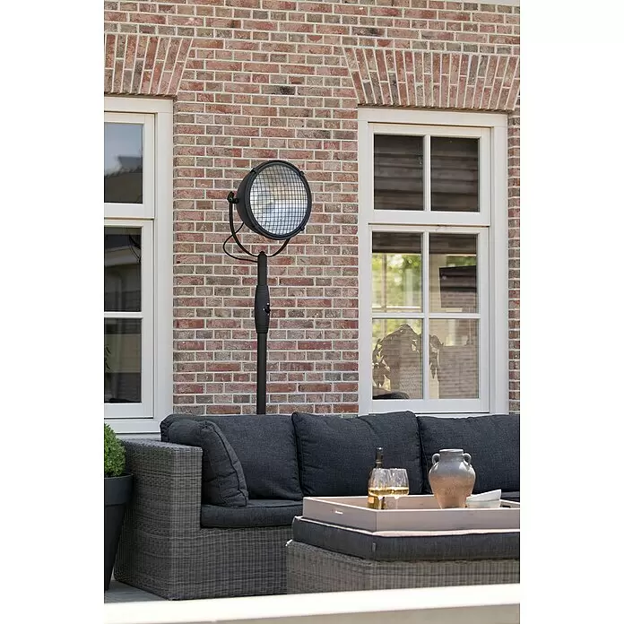 Sunred Halogen-Heizstrahler Indus - Höhe: 210 cm, 2.100 W, Schwarz - Schwarzer Terrassenheizer mit Schutzgitter auf einem Ständer, neben einem dunkelgrauen Outdoor-Sofa auf einer Terrasse.