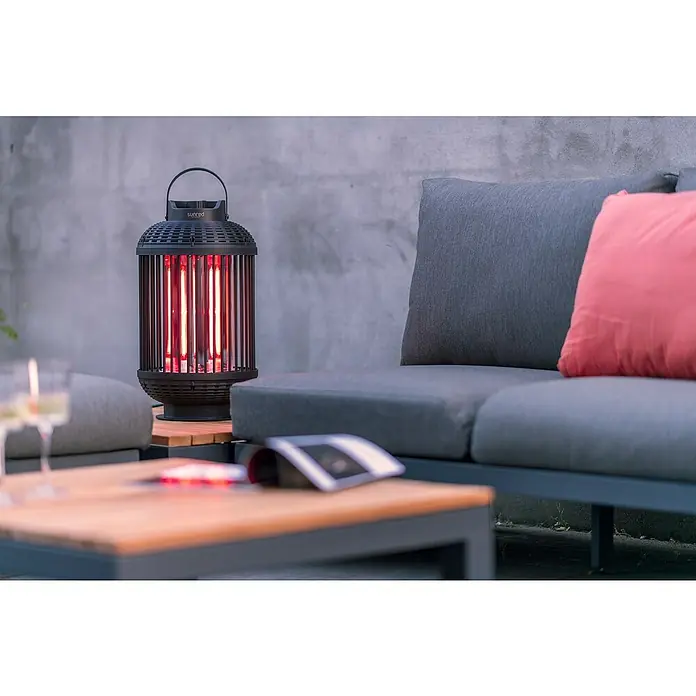 Sunred Heizstrahler Indox - Höhe: 59 cm, 1.200 W, Schwarz - Nahaufnahme einer Sunred Heizlaterne im Außenbereich, neben einem grauen Sofa mit einem roten Kissen, das eine gemütliche Atmosphäre schafft.
