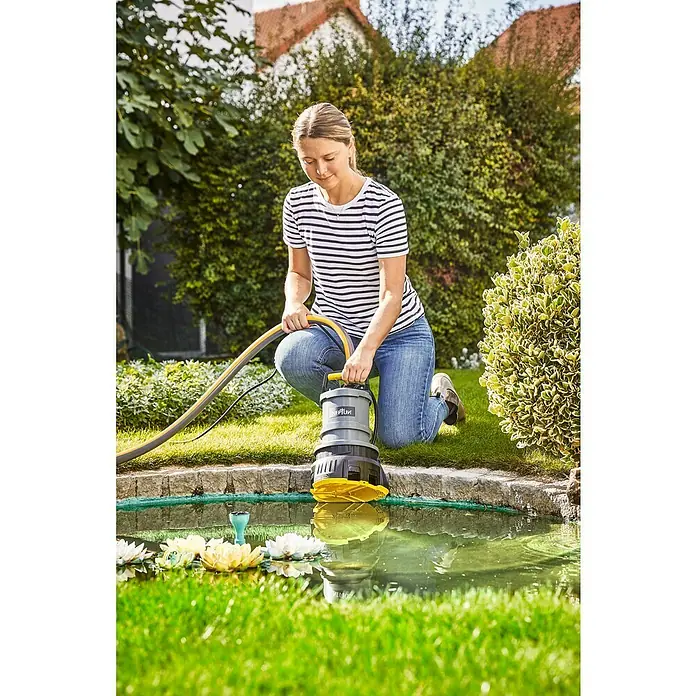 Neptun Abwasserpumpe NKSP-E 52 2in1 - 520 W, Max. Fördermenge: 13.500 l/h - Frau hockt an einem Teich und hält eine graue und gelbe Neptun-Pumpe. Die Pumpe wird zum Abpumpen von Wasser verwendet.