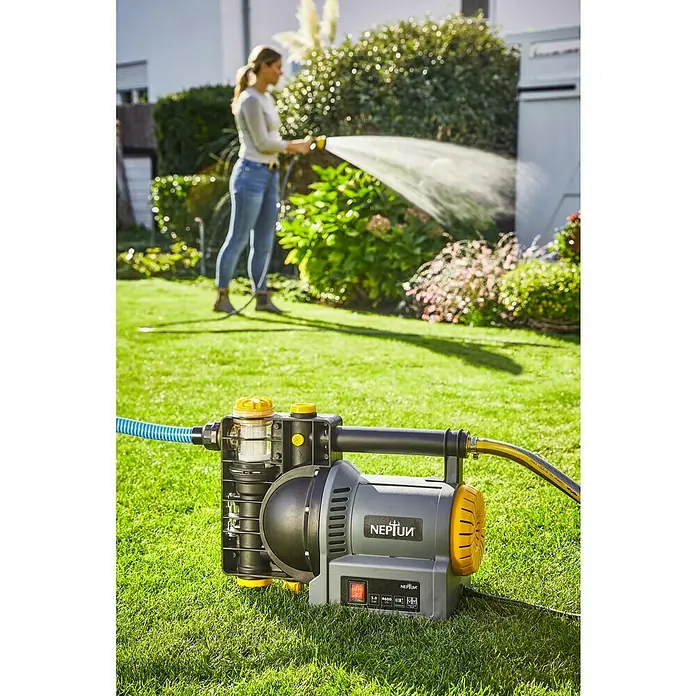 Neptun Gartenpumpe NGP-E 120 - 1.200 W, Max. Fördermenge: 4.600 l/h - Die NEPTUN Gartenpumpe auf einem Rasen mit einer Frau im Hintergrund, die mit einem Schlauch gießt. Ideal für die Gartenbewässerung.