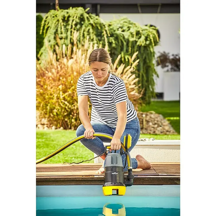 Neptun Bomba para aguas residuales NSP-E 75 - 750 W, Capacidad de bombeo máx.: 15.500 l/h, Profundidad de inmersión: 7 m - Una mujer opera una bomba sumergible NEPTUN gris y amarilla al borde de una piscina, con una manguera amarilla.