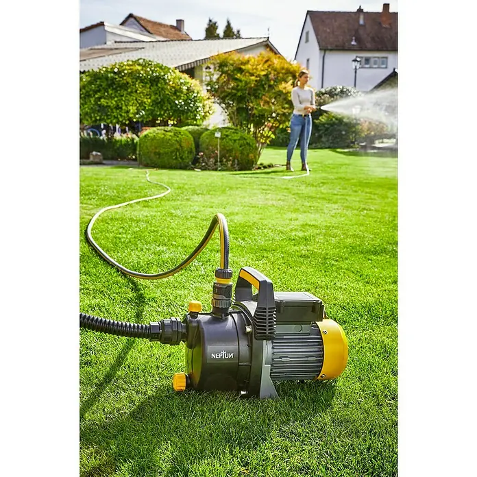 Neptun Bomba de agua para jardín NGP-E 68 - 680 W, Capacidad de bombeo máx.: 3.800 l/h, Altura de aspiración máx.: 8 m - Bomba de jardín NEPTUN sobre césped con manguera amarilla, mientras una mujer riega al fondo.