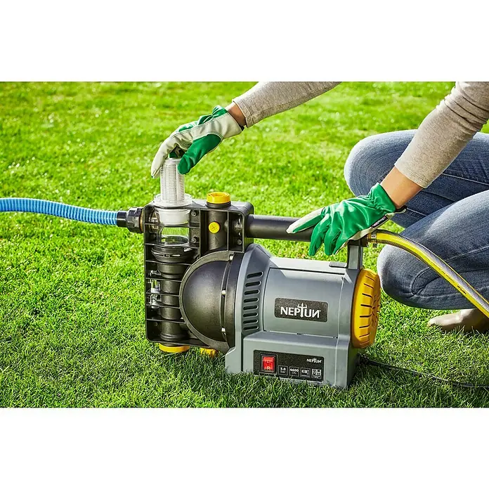 Neptun Gartenpumpe NGP-E 120 - 1.200 W, Max. Fördermenge: 4.600 l/h - Eine Gartenpumpe der Marke Neptun wird auf einem Rasen aufgestellt und von einer Person mit Gartenhandschuhen bedient.