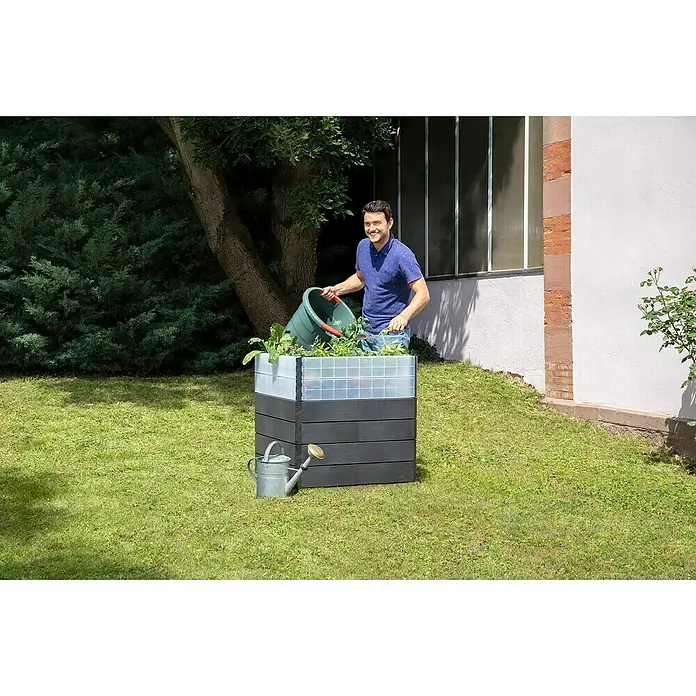 Garantia Hochbeet Ergo Quadro Turbo L Wood - Set - 80 x 80 x 75 cm, Kunststoff, Anthrazit/Braun - Ein Mann gießt Pflanzen in einem Hochbeet im Garten. Das Beet besteht aus dunklen Holzplanken und transparenten Gittern.