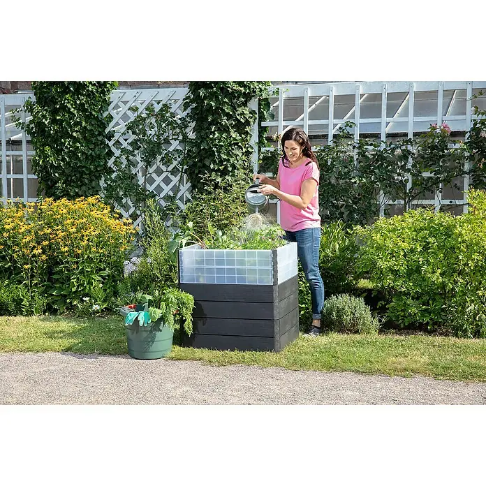 Garantia Hochbeet Ergo Quadro Turbo M Wood - Set - 60 x 80 x 75 cm, Kunststoff, Anthrazit/Braun - Frau gießt Gemüse in einem Hochbeet mit transparentem Aufsatz.