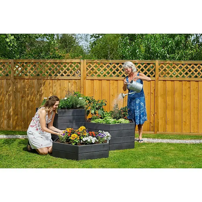 Garantia Hochbeet Ergo Vario 1 Wood - 190 x 190 x 75 cm, Kunststoff, Anthrazit/Braun - Frau gießt Pflanzen in grauen Pflanzkästen, während eine andere Frau sich um die Blumen kümmert. Holz Zaun im Hintergrund.