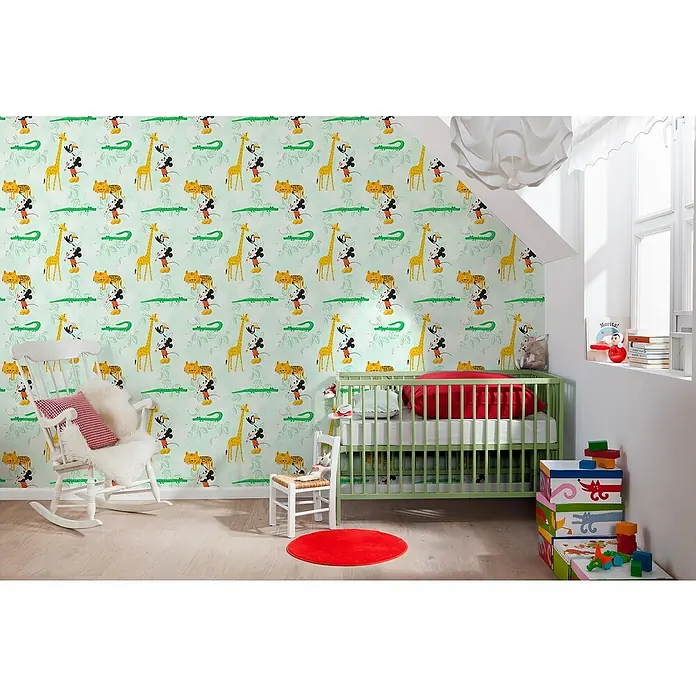 Komar Disney Edition 4 Vliestapete Mickey Mouse Doodle Zoo - Mehrfarbig, Grafisch, 10,05 x 0,53 m - Kinderzimmer mit grünem Gitterbett und weißem Schaukelstuhl vor auffälliger Tiermuster-Tapete, die eine spielerische und kindgerechte Atmosphäre schafft.