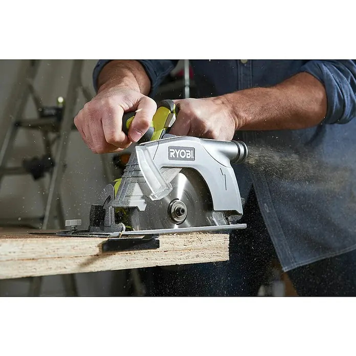 Ryobi ONE+ Akku-Handkreissäge R18CS-0 - 18 V, Ohne Akku, Leerlaufdrehzahl: 4.700 U/min - Nahaufnahme einer RYOBI Kreissäge in Aktion, die durch ein Holzbrett schneidet und dabei Sägemehl aufwirbelt. Die Hände des Bedieners sind sichtbar.