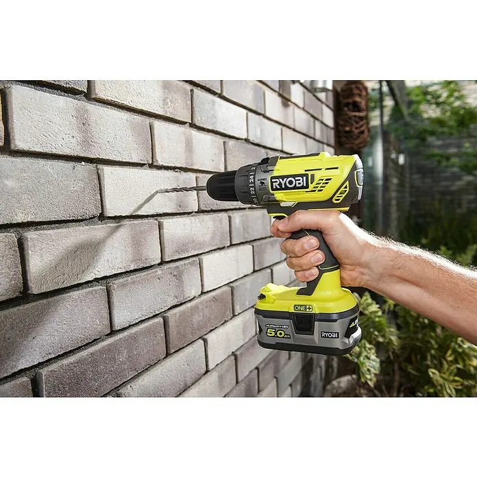 Ryobi ONE+ Taladro atornillador percutor de batería R18PD-0 - 18 V, Sin batería, 50 Nm - Primer plano de un taladro inalámbrico Ryobi perforando una pared de ladrillo, ideal para proyectos de bricolaje y construcción.