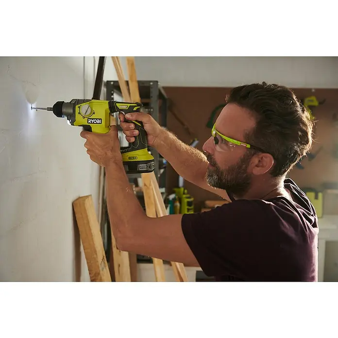 Ryobi ONE+ Akku-Kombihammer R18SDS-0 - 18 V, Ohne Akku, 1,3 J - Mann bohrt mit einer Ryobi Bohrmaschine ein Loch in eine Wand. Die Akku-Bohrmaschine ist gelb und schwarz.
