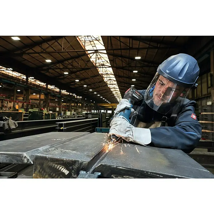 Bosch Professional AMPShare 18V Akku-Geradschleifer GGS 18V-23 PLC - 18 V, Ohne Akku, Leerlaufdrehzahl: 23.500 U/min - Ein Arbeiter in Schutzkleidung schleift Metall mit einem Winkelschleifer in einer Fabrikhalle, wobei Funken sprühen.