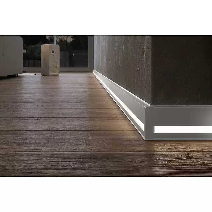 Deckprofil Cubica LS80 Light Down - Aluminium, 2,5 m x 19 mm x 80 mm - Graue Sockelleiste mit integrierter LED-Beleuchtung an dunkler Wand und Holzboden, den Raum beleuchtend.