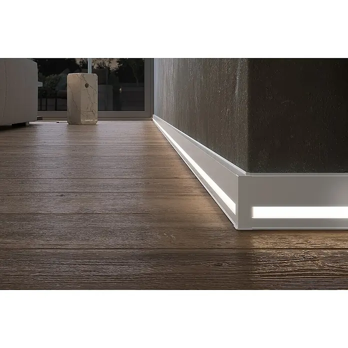 Deckprofil Cubica LS80 Light Down - Weiß, 2,5 m x 19 mm x 80 mm - Detailaufnahme einer modernen weißen Sockelleiste mit integrierter LED-Beleuchtung an einer Wand und Holzboden.