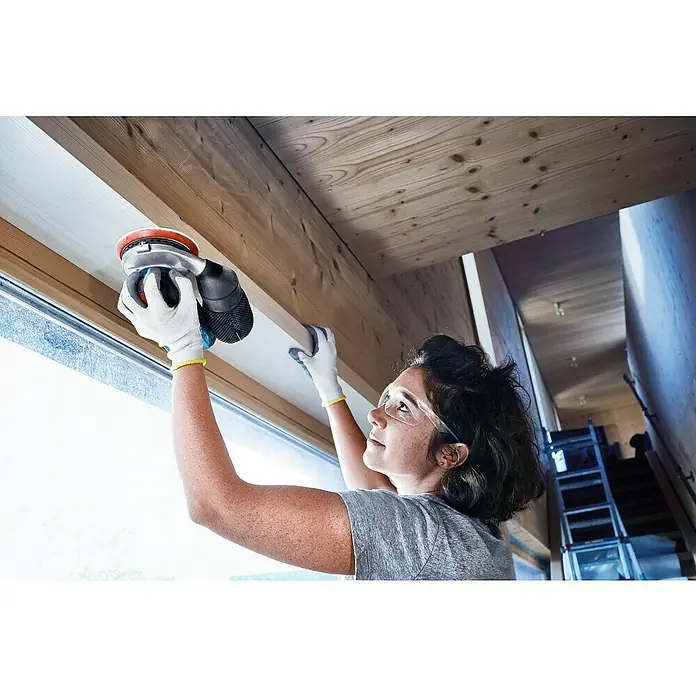Bosch Professional AMPShare 18V Akku-Exzenterschleifer GEX 18V-125 - 18 V, Ohne Akku, Durchmesser Schleifteller: 125 mm, Karton - Frau schleift Holz mit einem elektrischen Schleifgerät, Schutzbrille und Handschuhen für sichere Oberflächenbearbeitung.